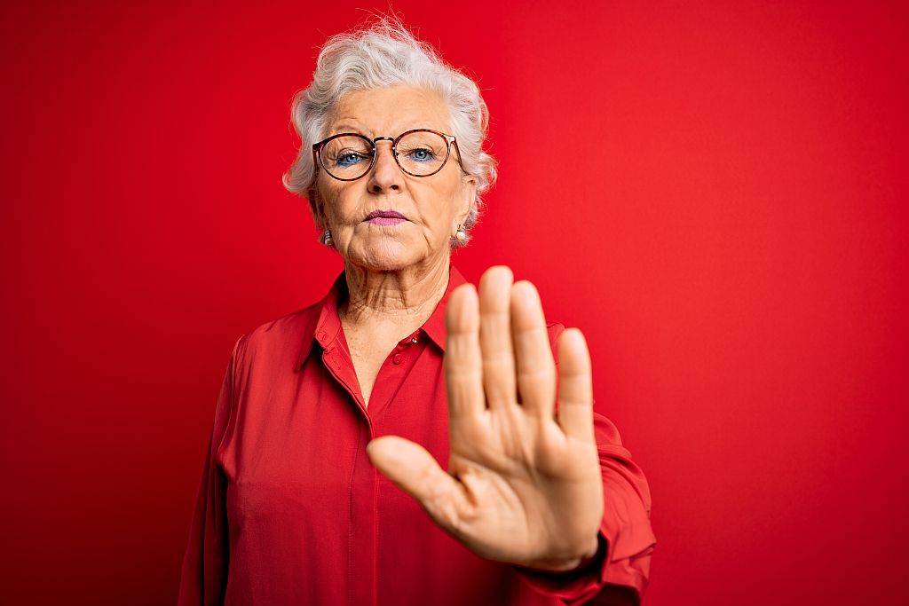 Senior beautiful grey-haired woman wearing casual shirt and glasses over red background doing stop sing with palm of the hand. Warning expression with negative and serious gesture on the face.