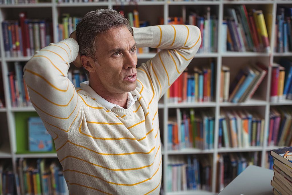 Lehrer erschöpft vor Bücherregal, Foto: Adobe Stock